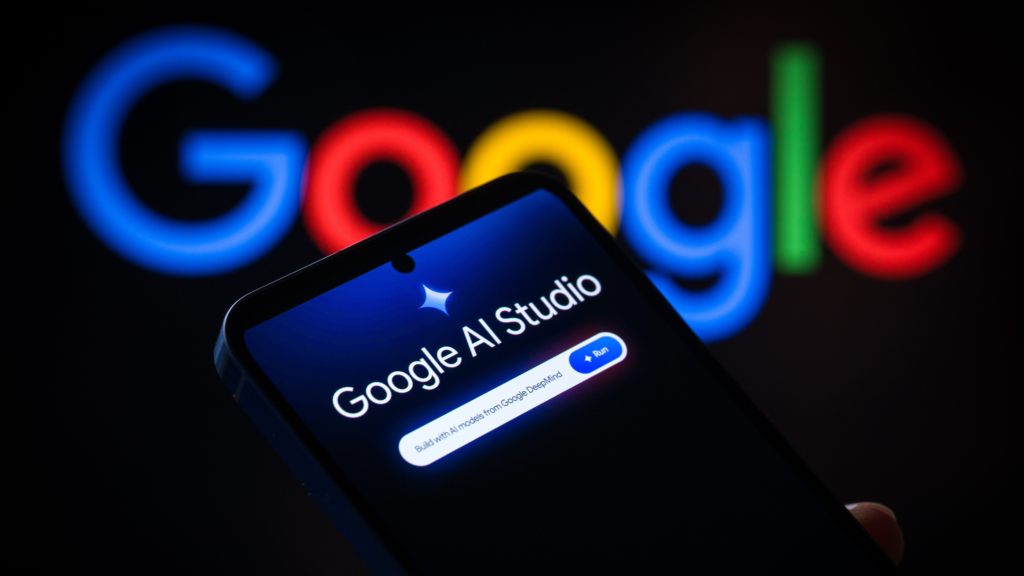 Sebuah telefon pintar memaparkan antaramuka Google AI Studio dengan logo warna-warni Google yang kabur di bahagian latar belakang.