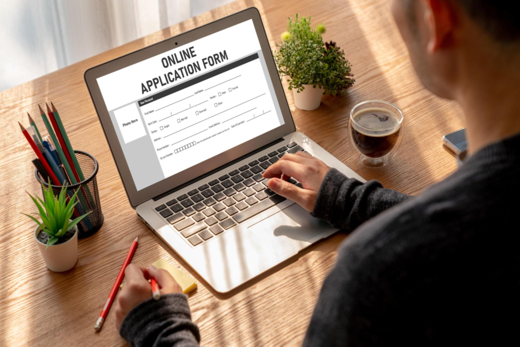 A person filling out an online application form on a laptop at a office desk.